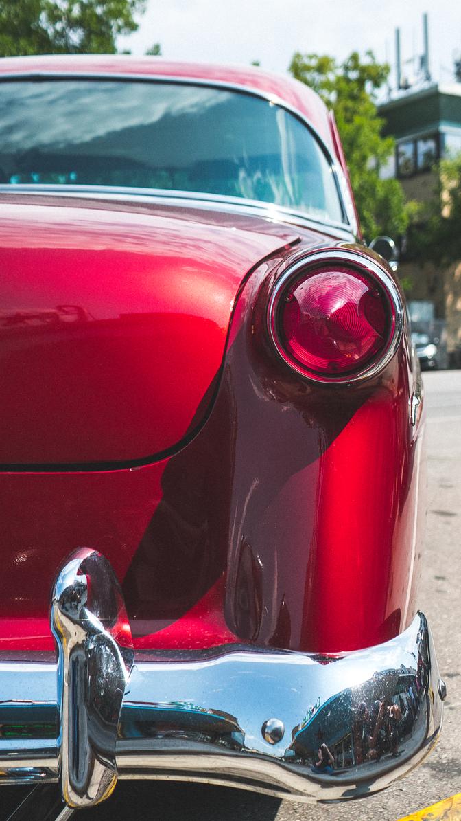 The taillight and rear bumper of a red classic car from a low angle