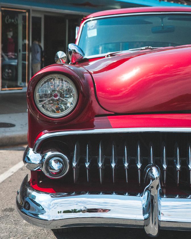 The grille and headlight of a red classic car in a parking space downtown