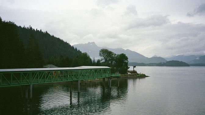 A green gangway leading to a small visitor's center on the coast of Alaska, with hazy mountainscape on the horizon